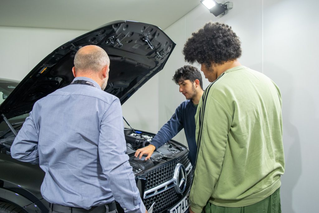 a man showing 2 students the engine of a car