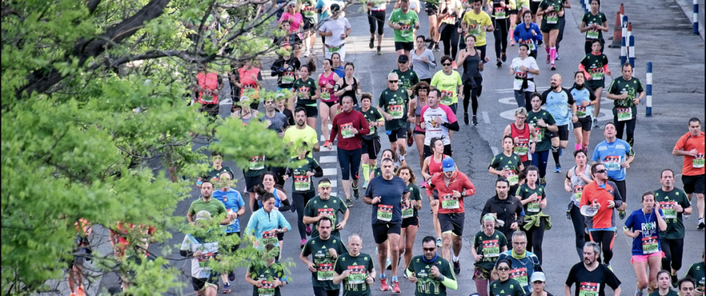 Aerial shot of runners competing in the London Marathon, wearing brightly coloured bibs whilst running down a grey road.