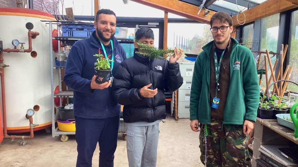 Tom stood with a staff member and student in the greenhouse at Bridge College.