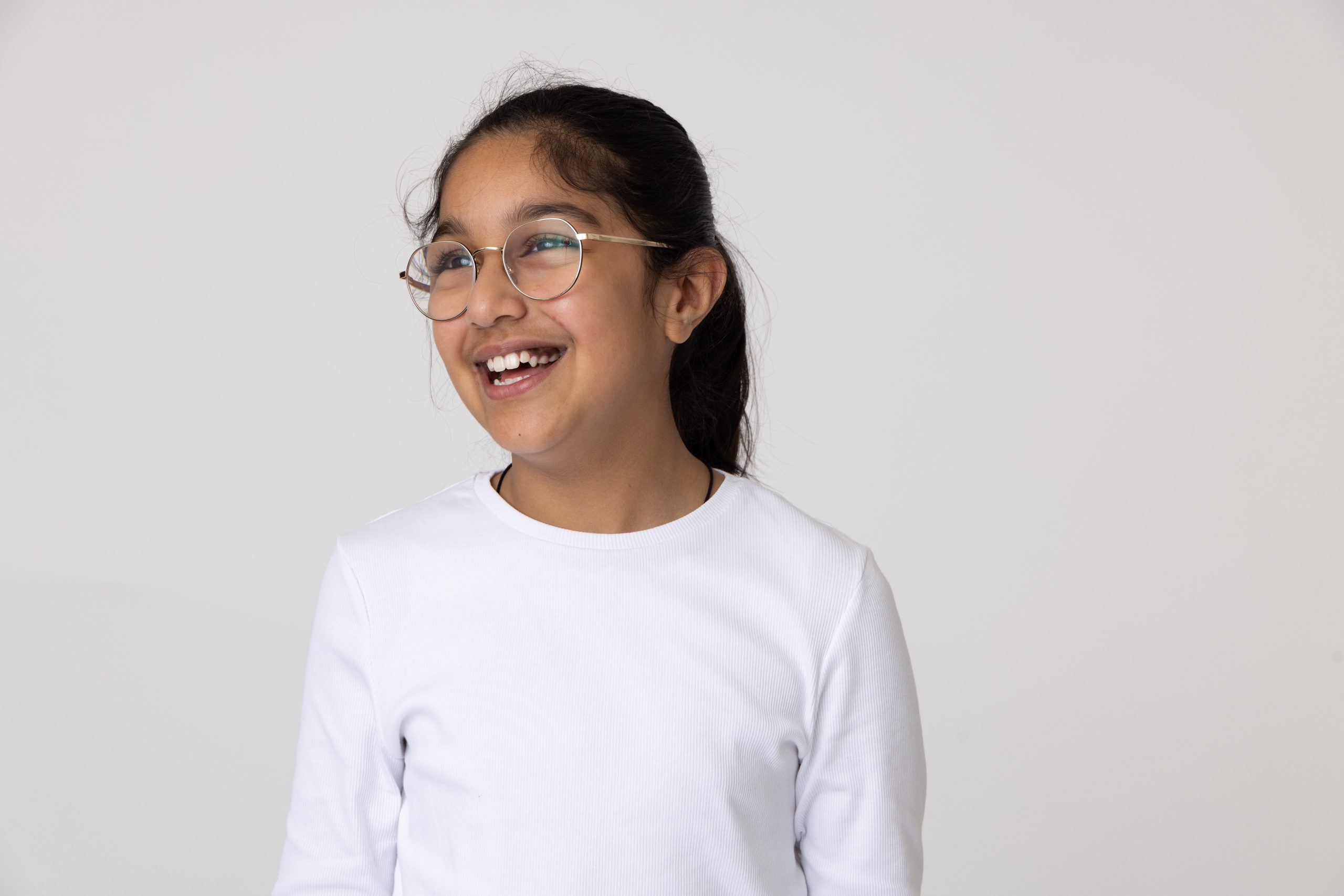 School aged girl wearing glasses smiling broadly and looking to the side