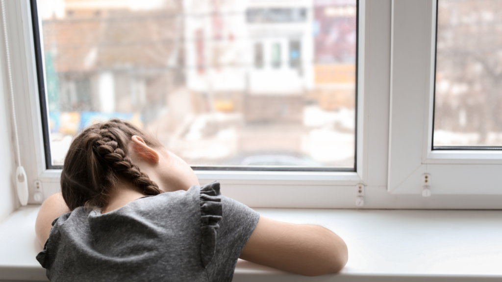 Girl resting her head on a windowsill, looking sadly out of the window.