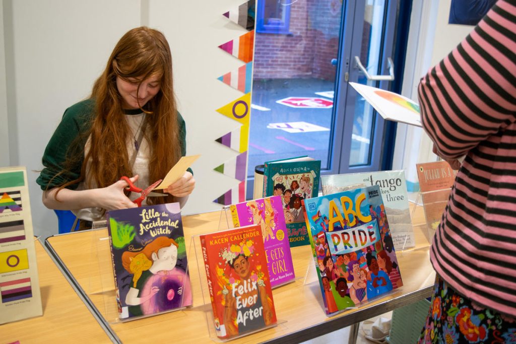 Teen girl sitting behind a table full of books on LGBTQ+ topics.