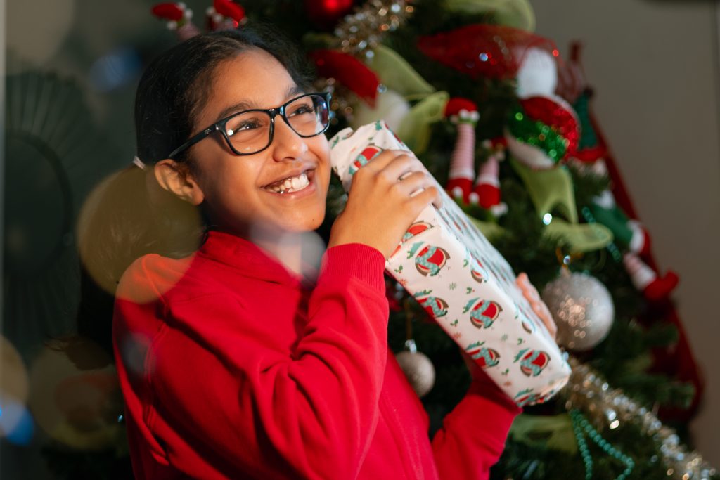 a young girl in a red jumper smiling holding a wrapped Christmas present