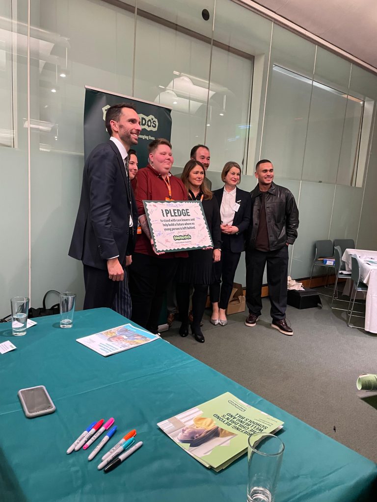 Group of people holding up a banner that reads "I pledge to stand with care leavers and help build a future where no young person is left behind". On the banner there are lots of signatures from the people present at the conference.