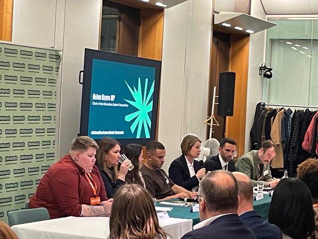 A group of 7 people sitting at a table together talking to a room of people watching them. 