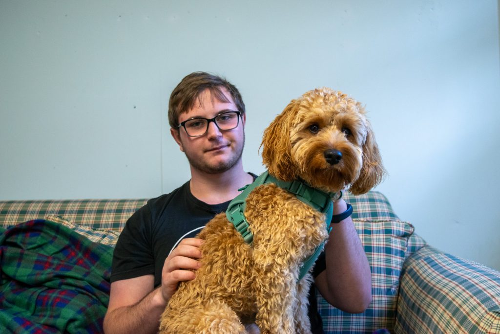 Jack, a teen, is holding the dog, a golden doodle, in his lap. He is stroking the dog's back.