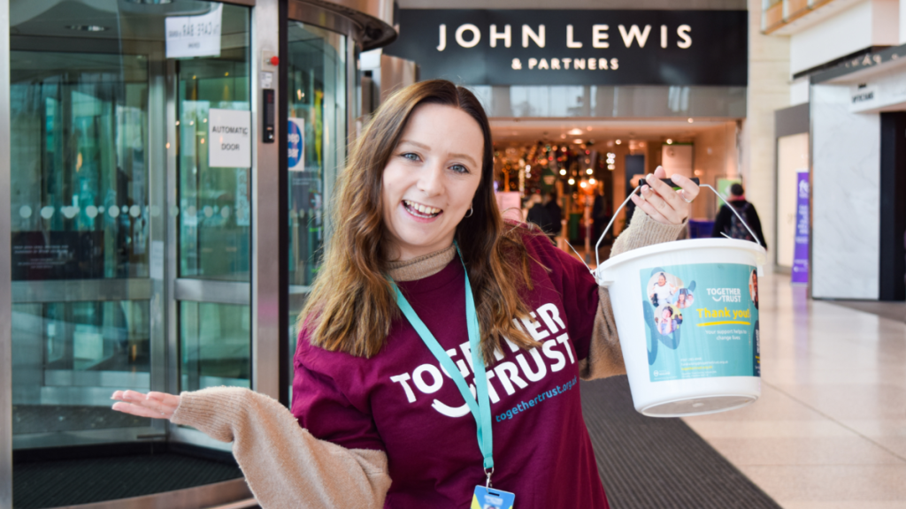 a member of staff smiling holding a donation bucket