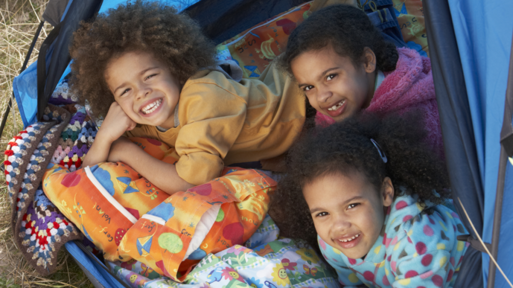 a group of three children smiling at the camera laying in a tent