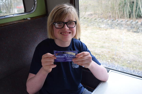 A young boy smiling holding a train ticket.