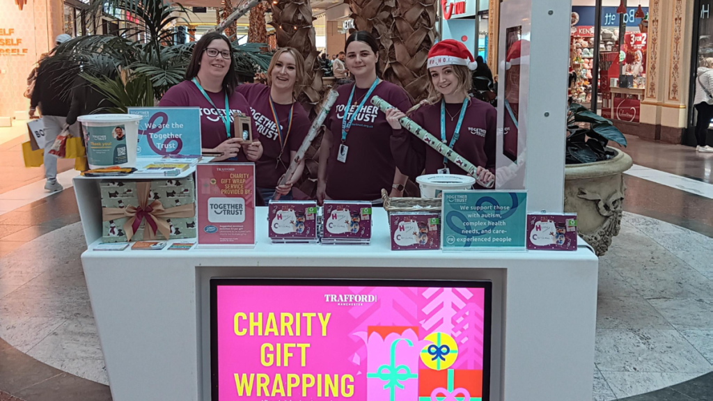 four fundraising staff members stood behind a table that reads 'charity gift wrapping'