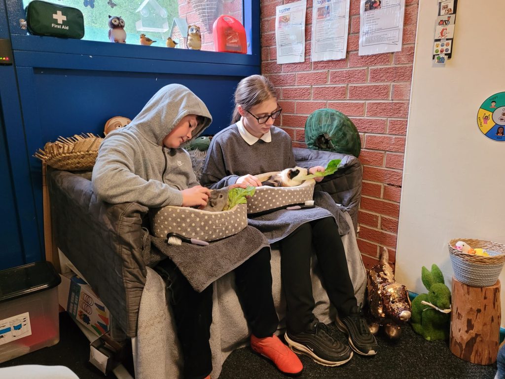Two students sat on a small sofa each holding a guinea pig.