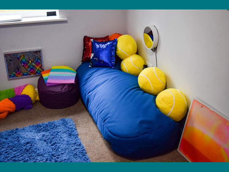  A photo of one of the bedrooms at Haines House. Showing a large blue cushion with smaller yellow cushions. 