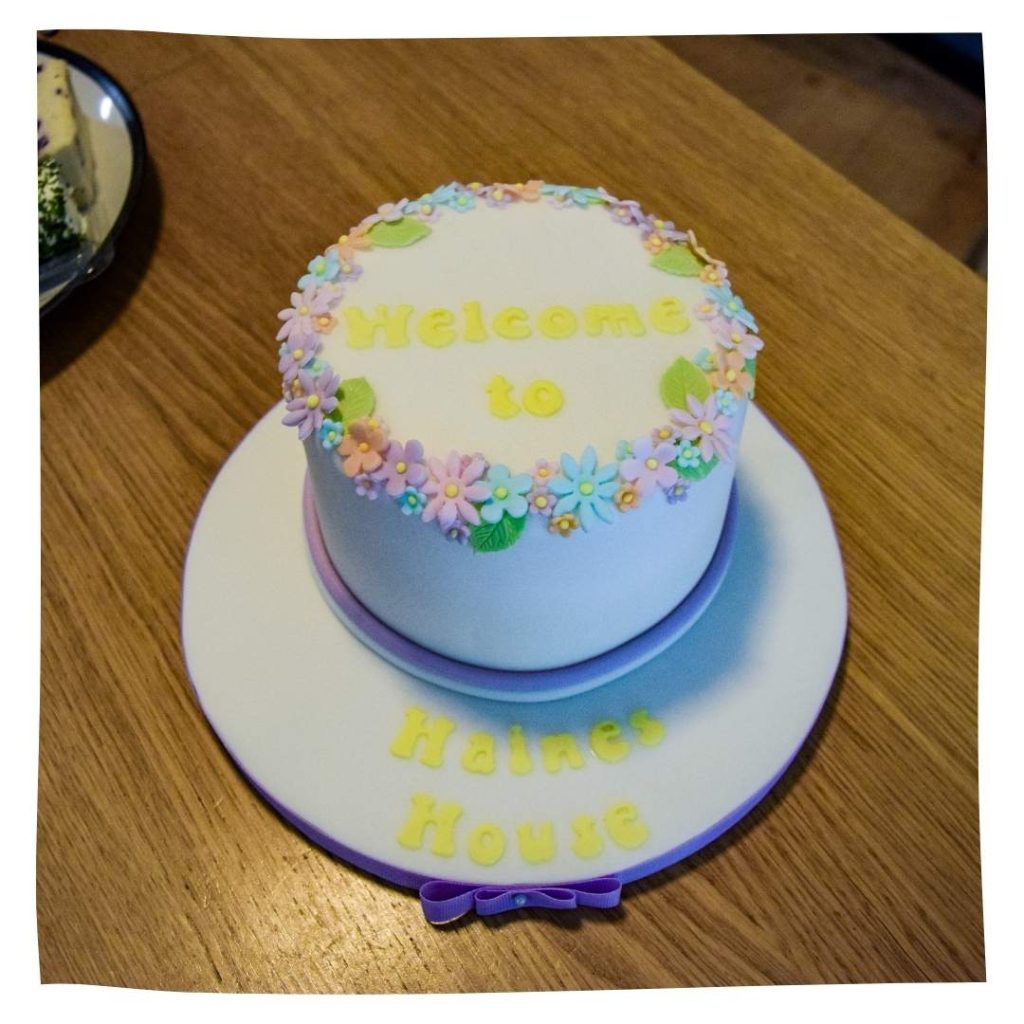 A white cake that says 'welcome to Haines House' on it in yellow.