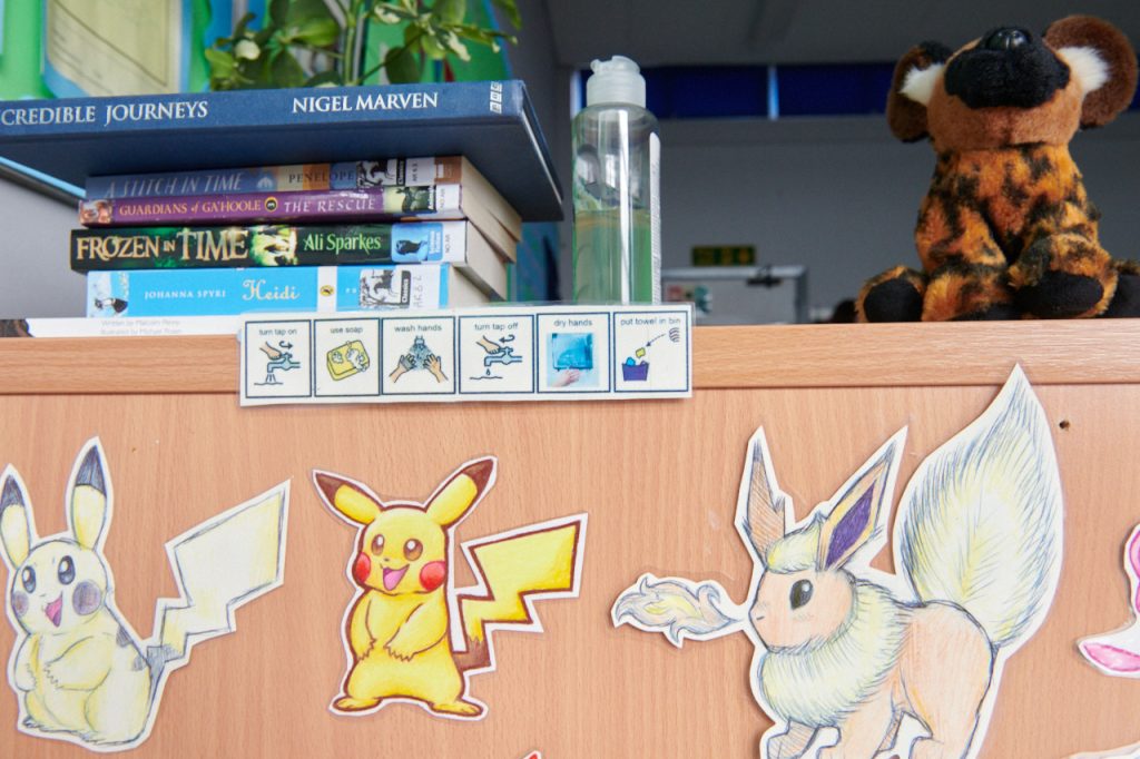 A child's desk at school that shows stickers of pokemon characters and a PECS symbol schedule.