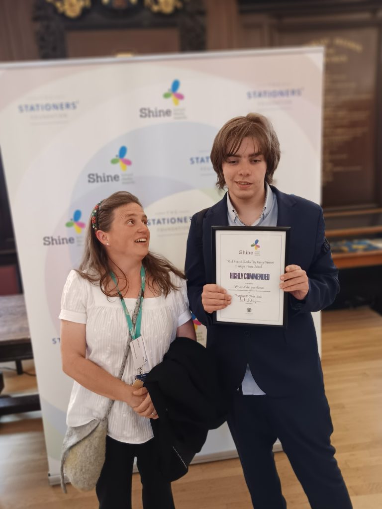 Judit, associate teacher is posing next to Harry in front of a banner. Harry is holding his certificate.
