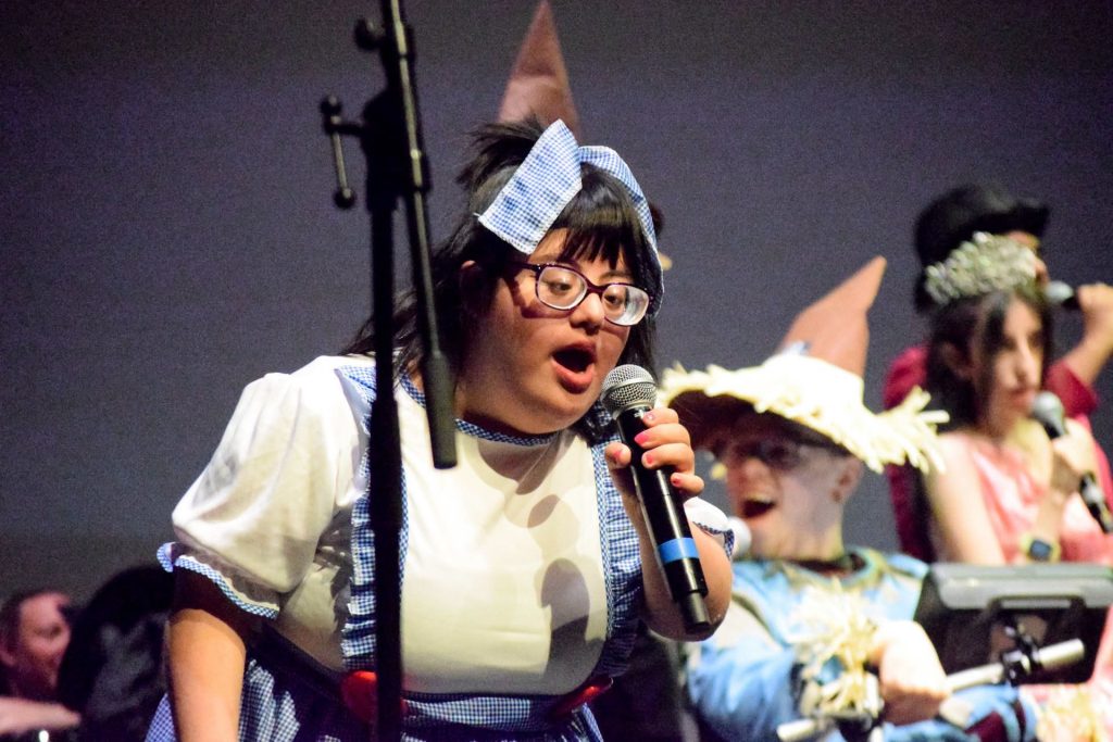 A young woman dressed like Dorothy is singing with a microphone on the stage