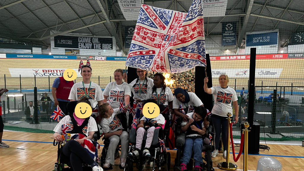 A photo of a group of students dressing in union jack flags. They are stood in the Manchester velodrome with the cycling track behind them.