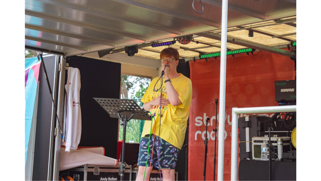 James on a stage wearing a yellow t-shirt holding a microphone singing
