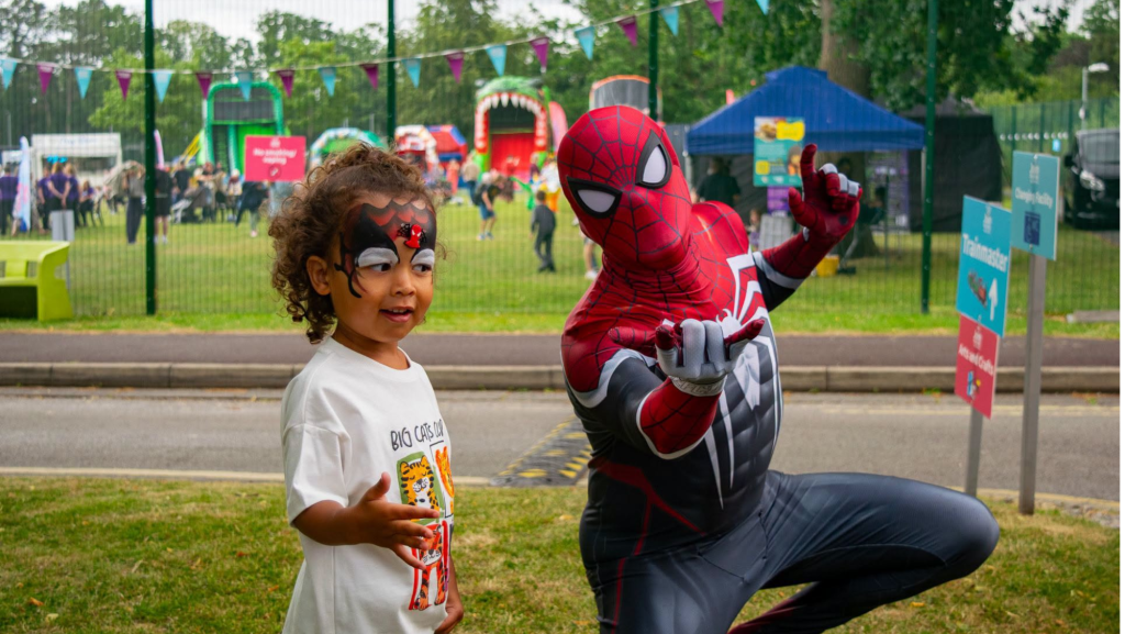 A photo of Spiderman with a young child with wearing Spiderman face paint. They are striking the web throwing pose.