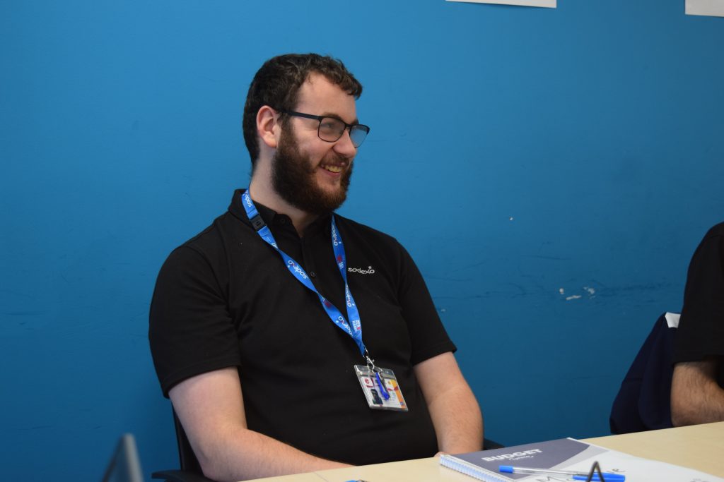 McKenzie, a young man, is sitting at a table smiling.
