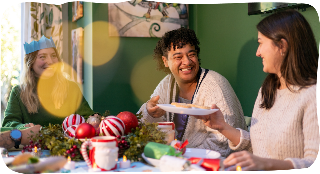 Three young people sitting around the table smiling and having Christmas themed food