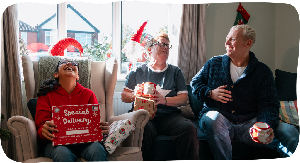 Three people laughing and smiling and opening Christmas presents