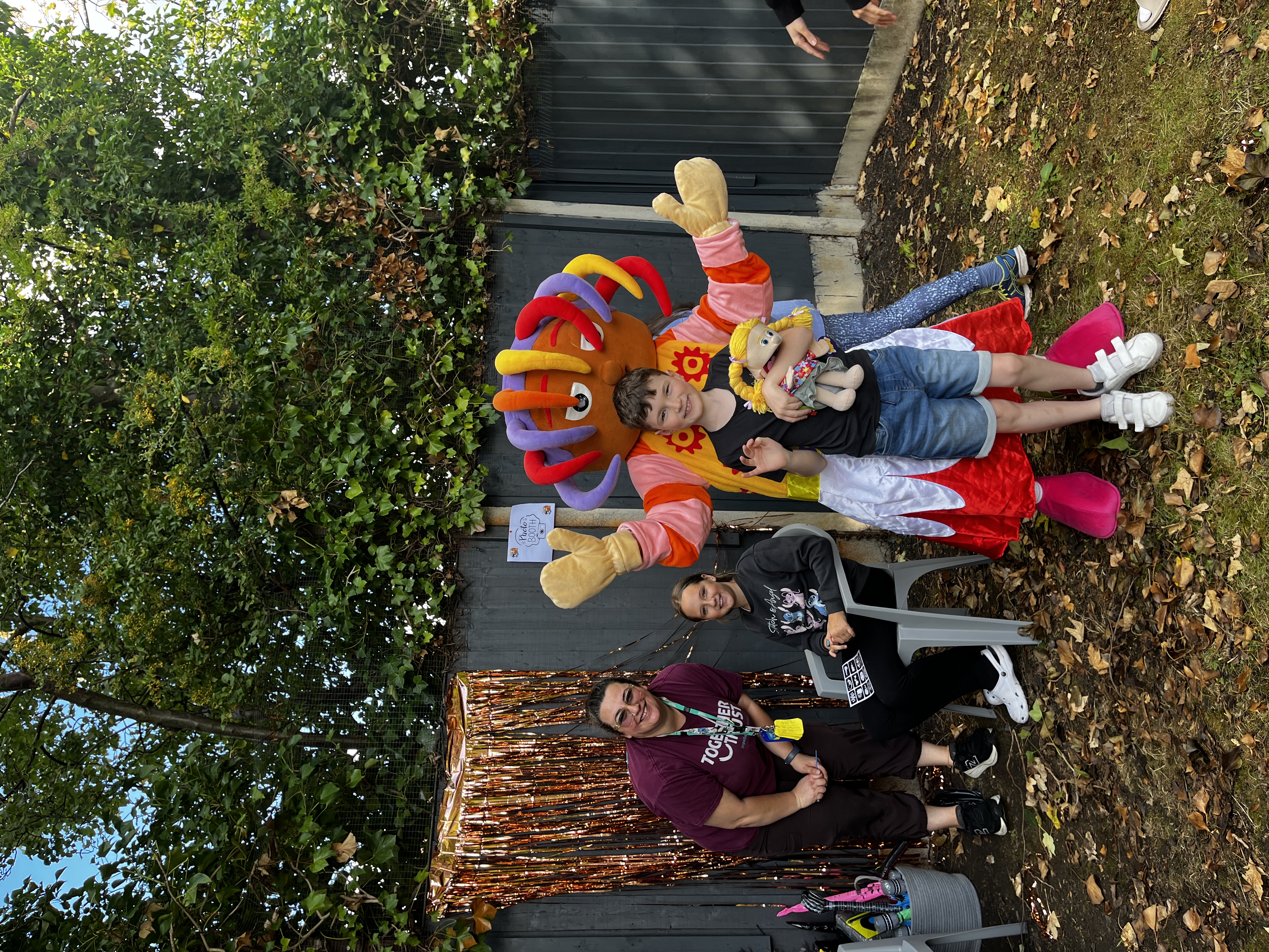 A staff member and two children posing next to an Oopsie Daisy mascot.