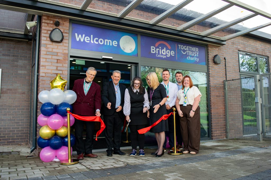 A group of staff members, trustees, Eamonn O’Neal and Dana cutting a ribbon outside of the school entrance. 