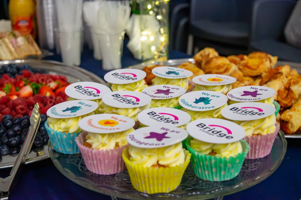 A platter of cupcakes decorated with edible paper that has the Bridge College logo on.