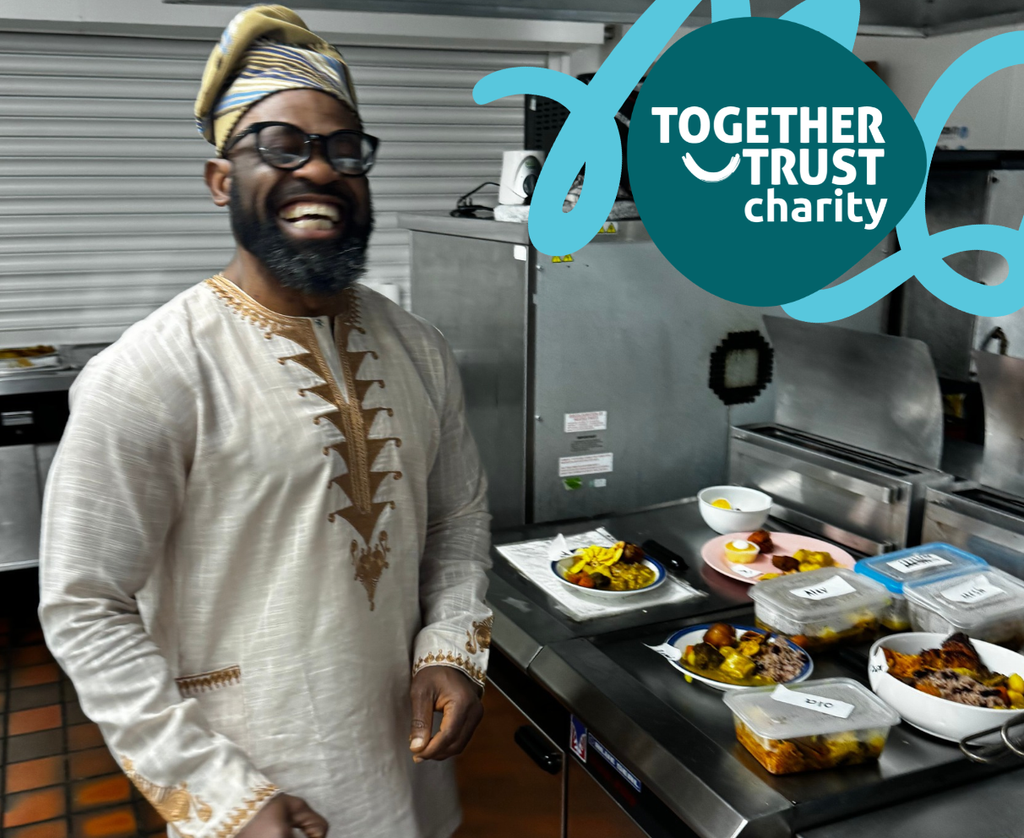 Salford Hub colleague standing in front of a buffet of food in a kitchen. He is laughing and smiling.