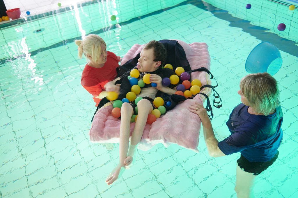 a student floating in a pool with coloured balls all around them