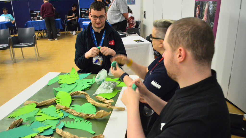 A photograph of three people sat at a table creating a jungle scene out of paper and clay