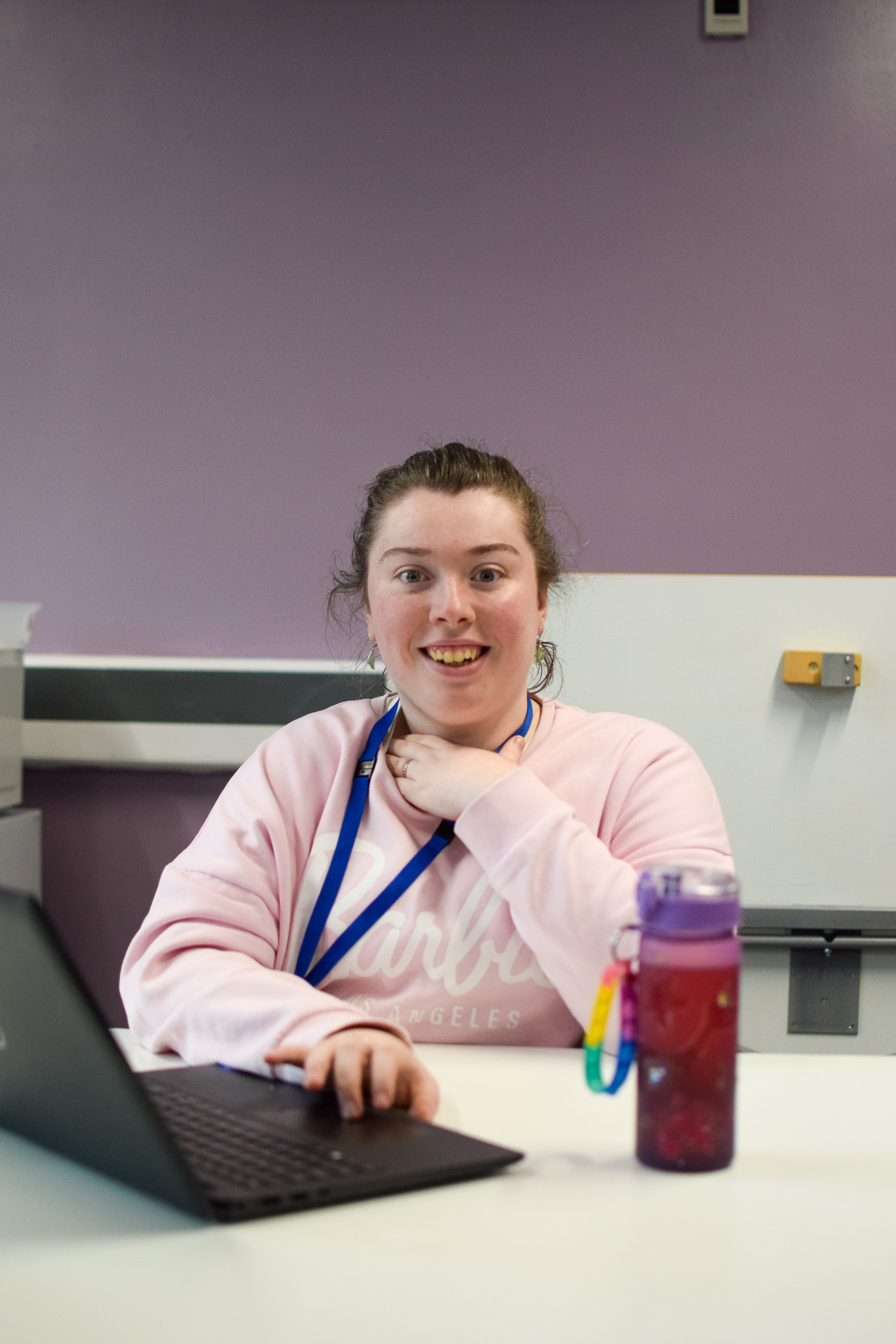 A young woman smiles at the camera as she is working on a computer in a classroom.