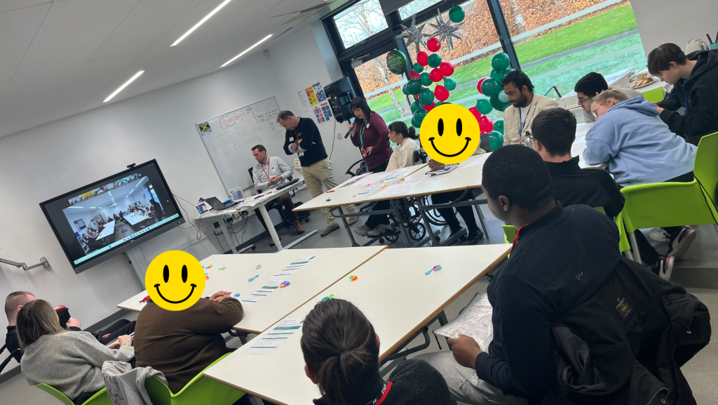 students sitting around tables looking at a zoom call with other students