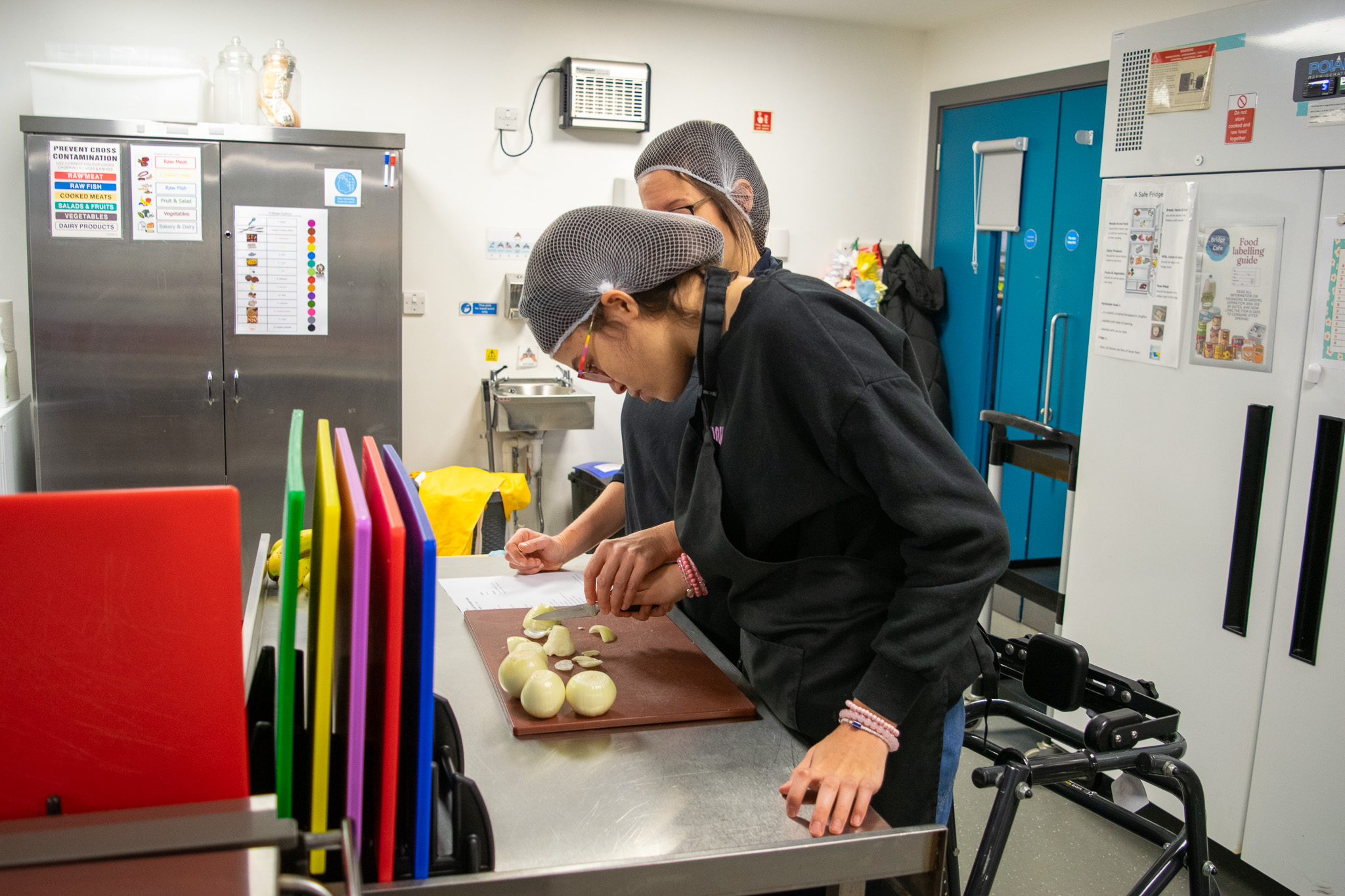 A young woman is chopping onions in an industrial kitchen at College.