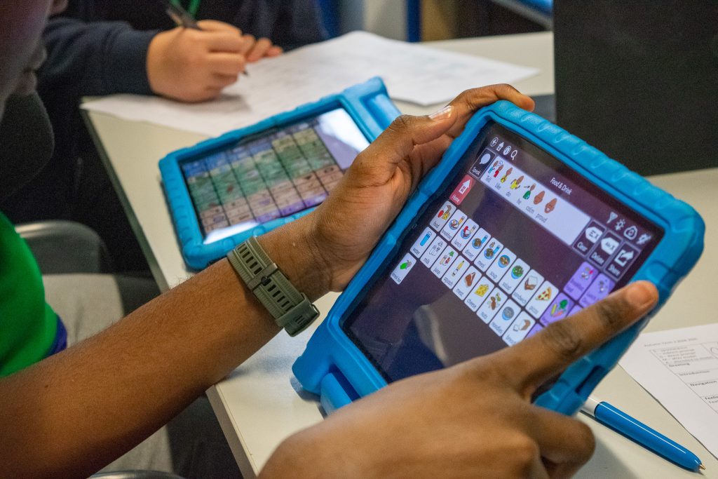Two young people operate alternative communication devices.