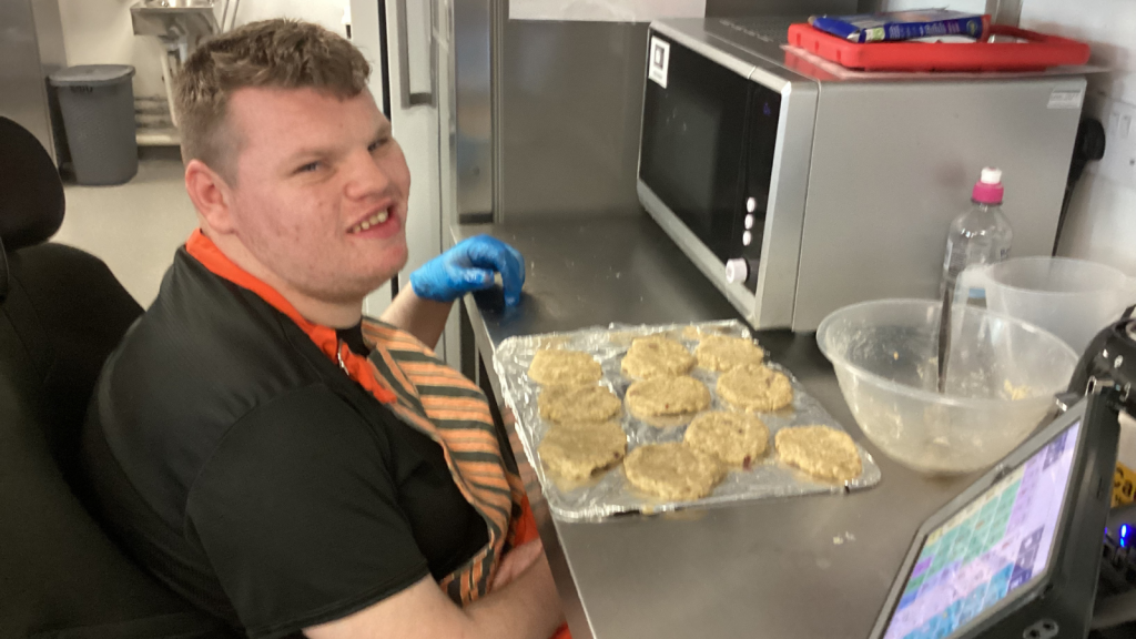 A young man is lining up burger patties to be put in the oven. 