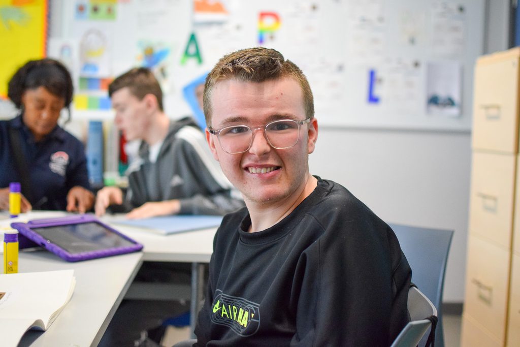 A young man smiling at the camera in a colorful classroom.