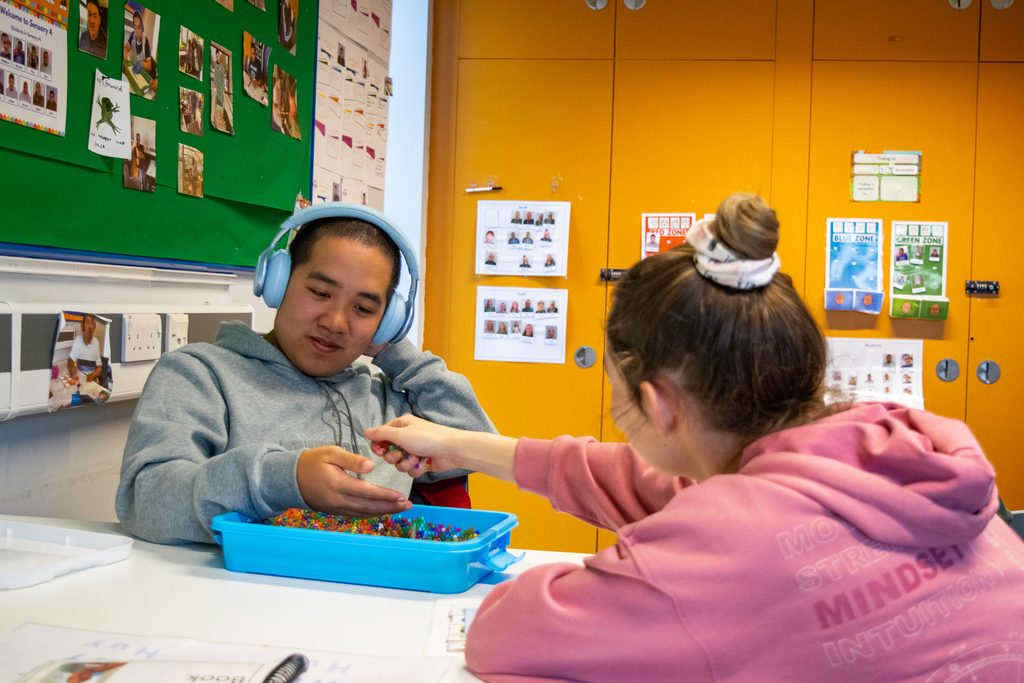 A teacher is helping a young man play with sensory toys.