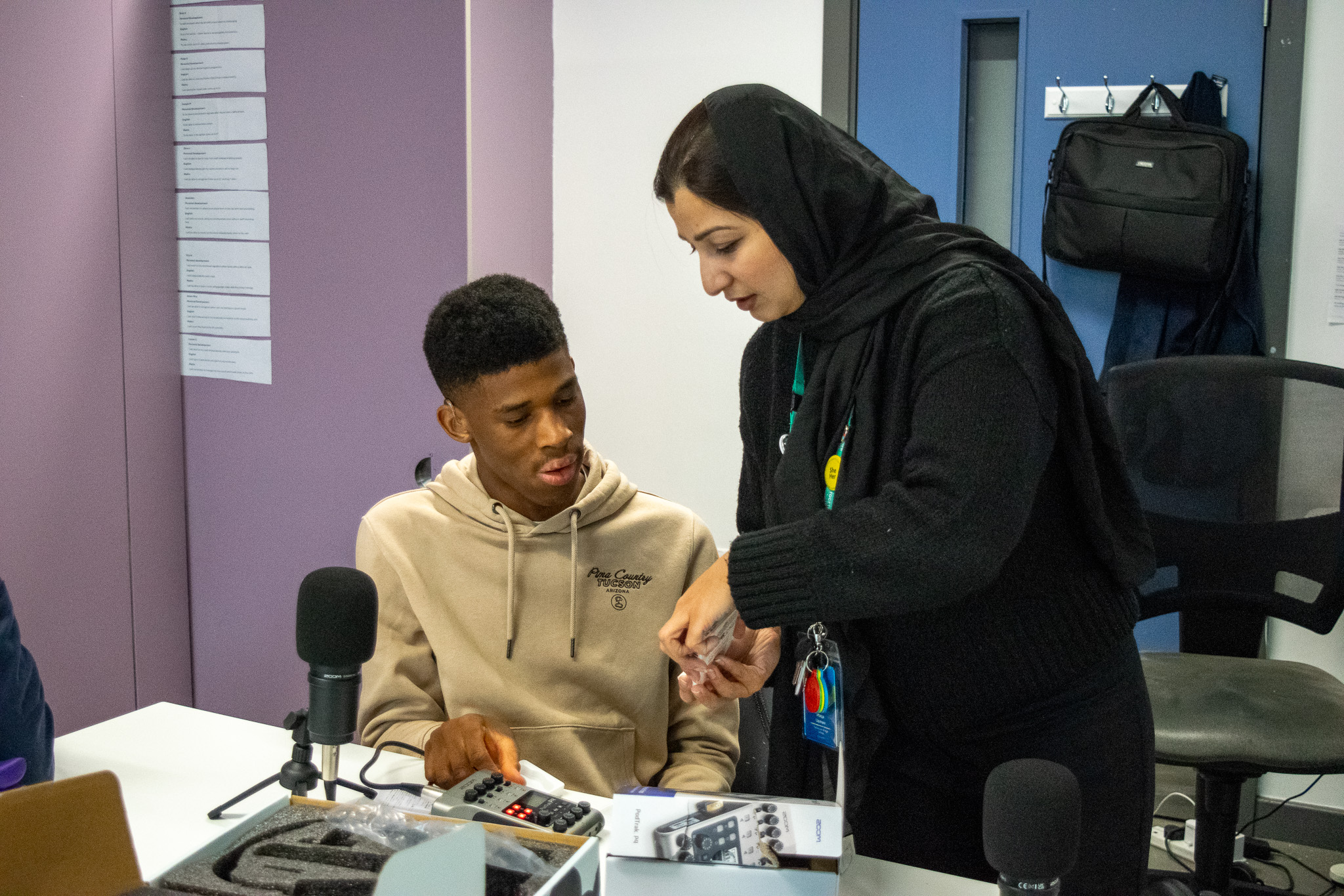 A teacher is showing a young man how to operate tech equipment for podcast recording.