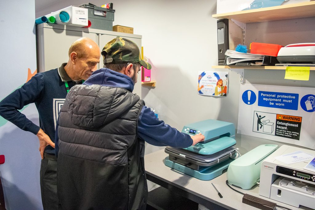 A young man is using a printing press in the enterprise room to print text onto a tote bag.