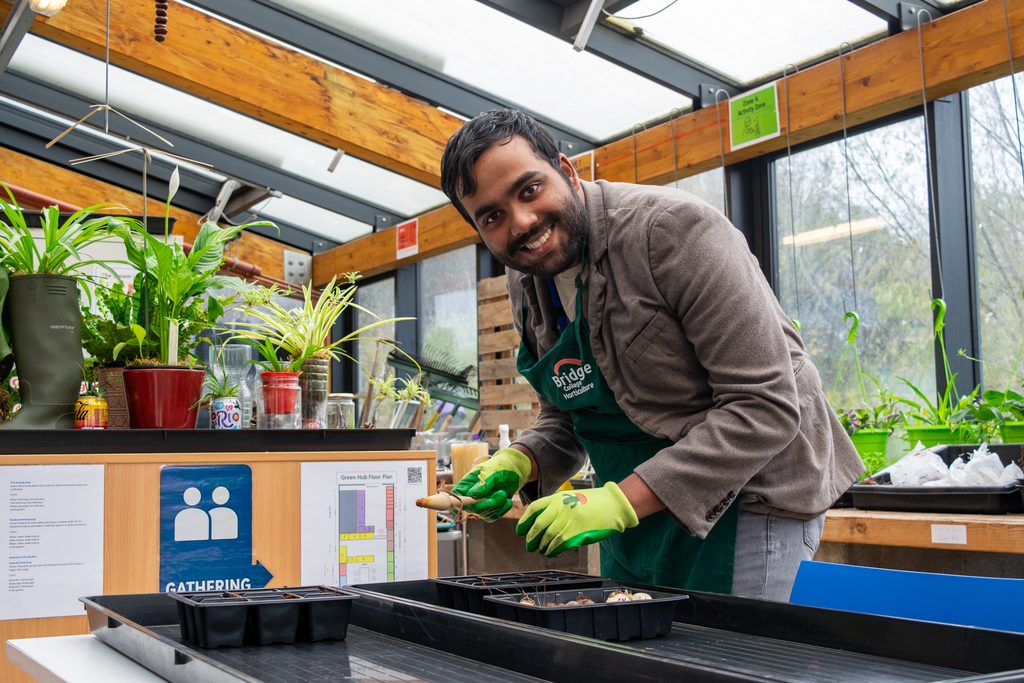 A young man is smiling at the camera as he is in horticulture class, planting bulbs