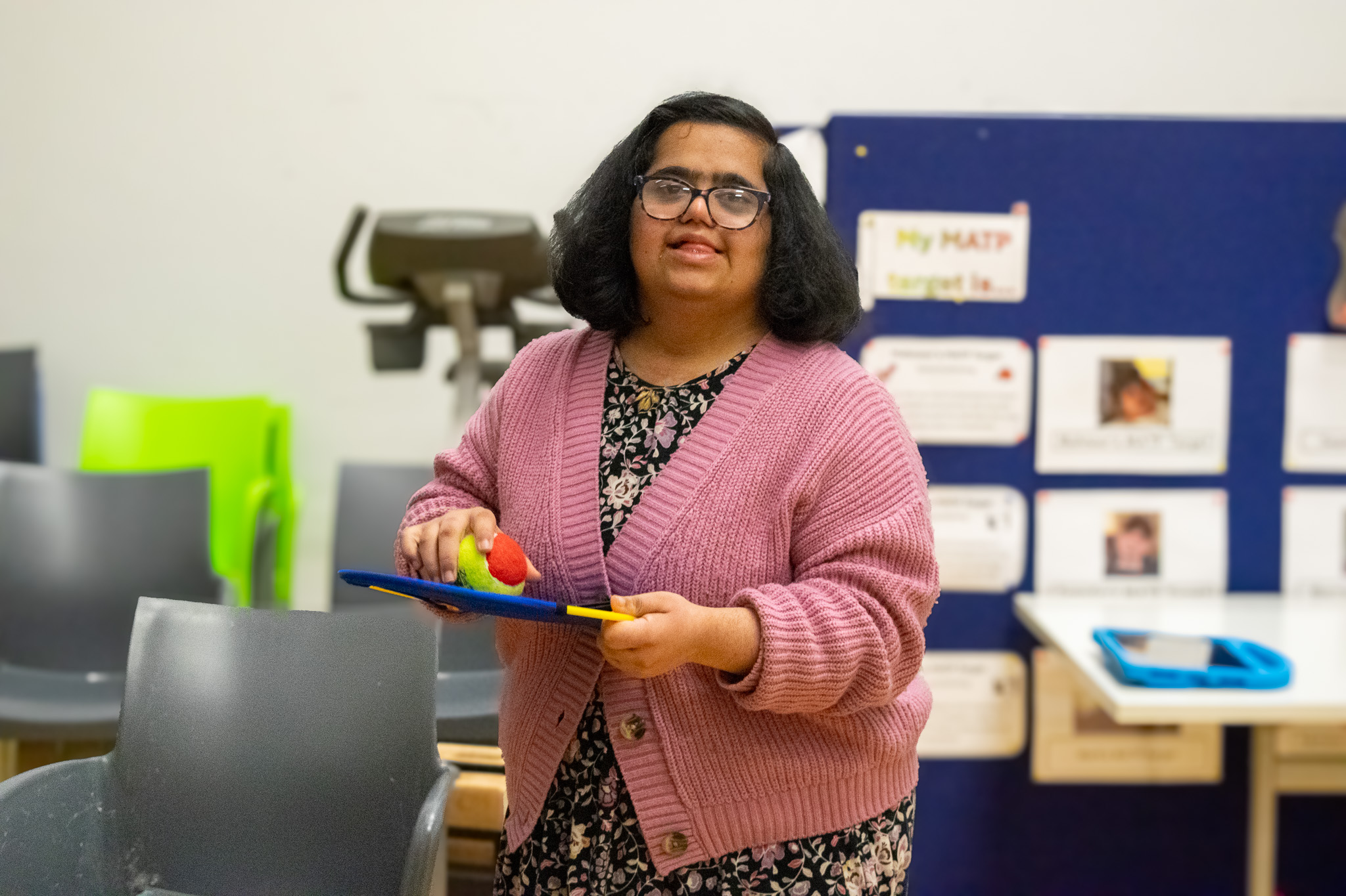 A young woman with down syndrome in gym class playing with a ball with velcro and a mat to catch it .