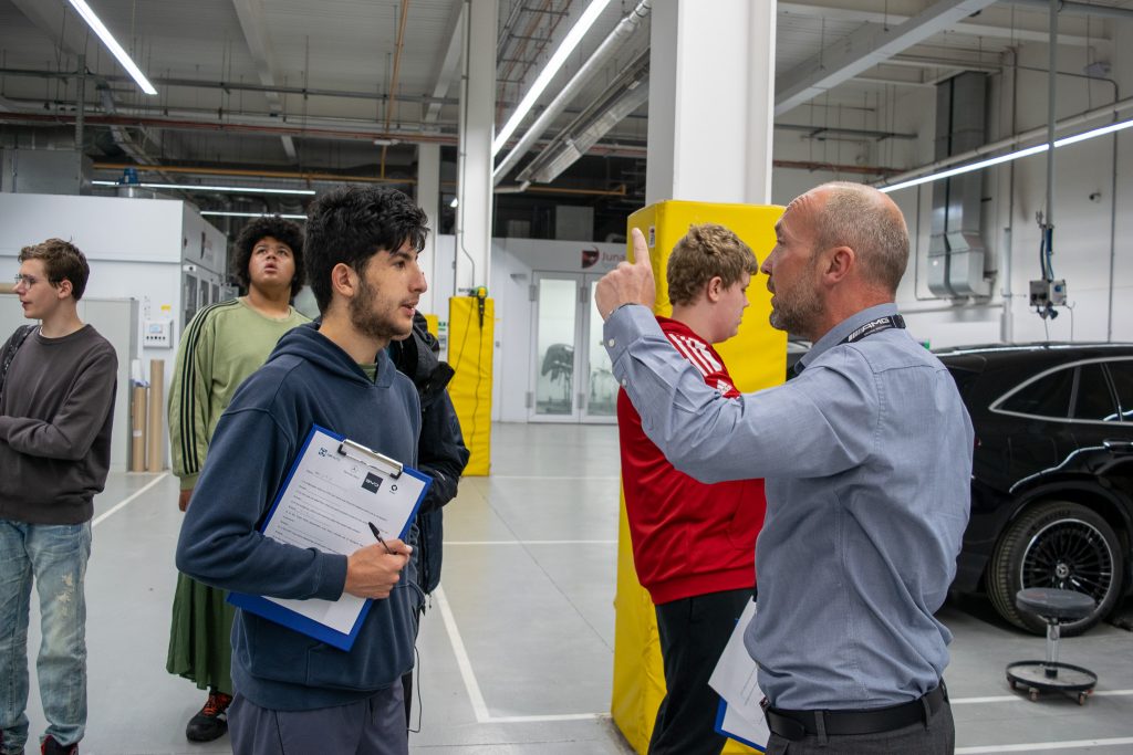 a group of students listening to a man talk to them about painting cars in the bodyshop 