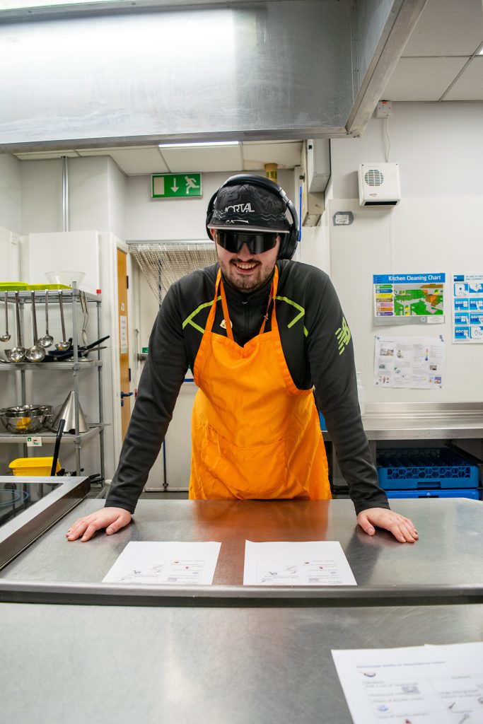 a student smiling at the camera wearing an orange apron 