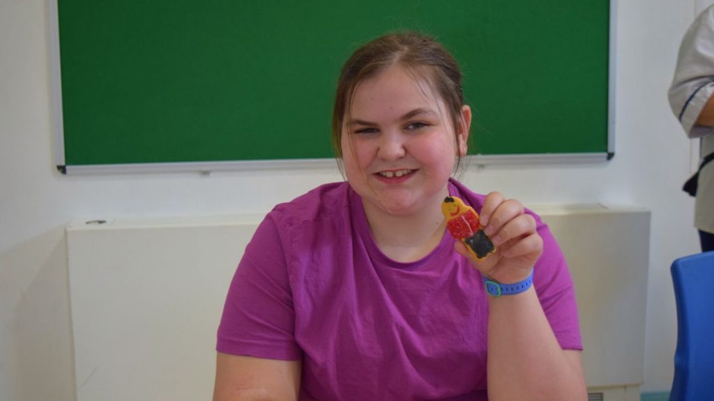 Student smiling and showing her decorated gingerbread biscuit to the camera.