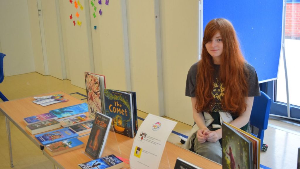 Talia, sitting at the book stall with a range of books.