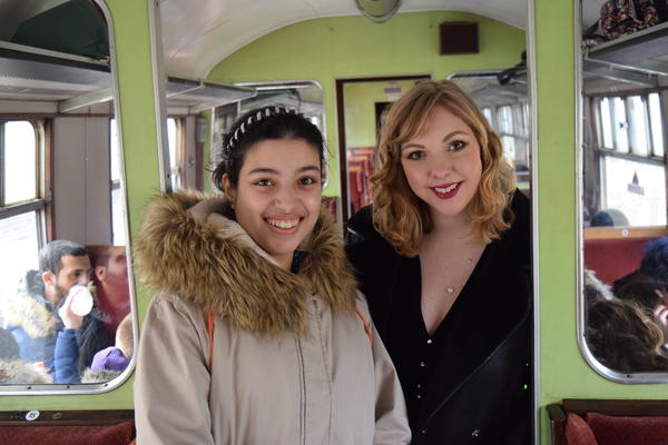 Two women smiling at the camera on board a train.
