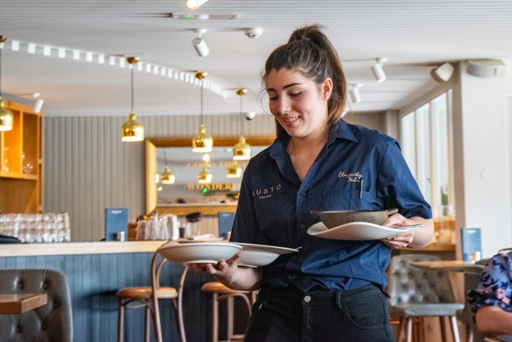 Teenage girl holding plates of food walking through the restaurant smiling.