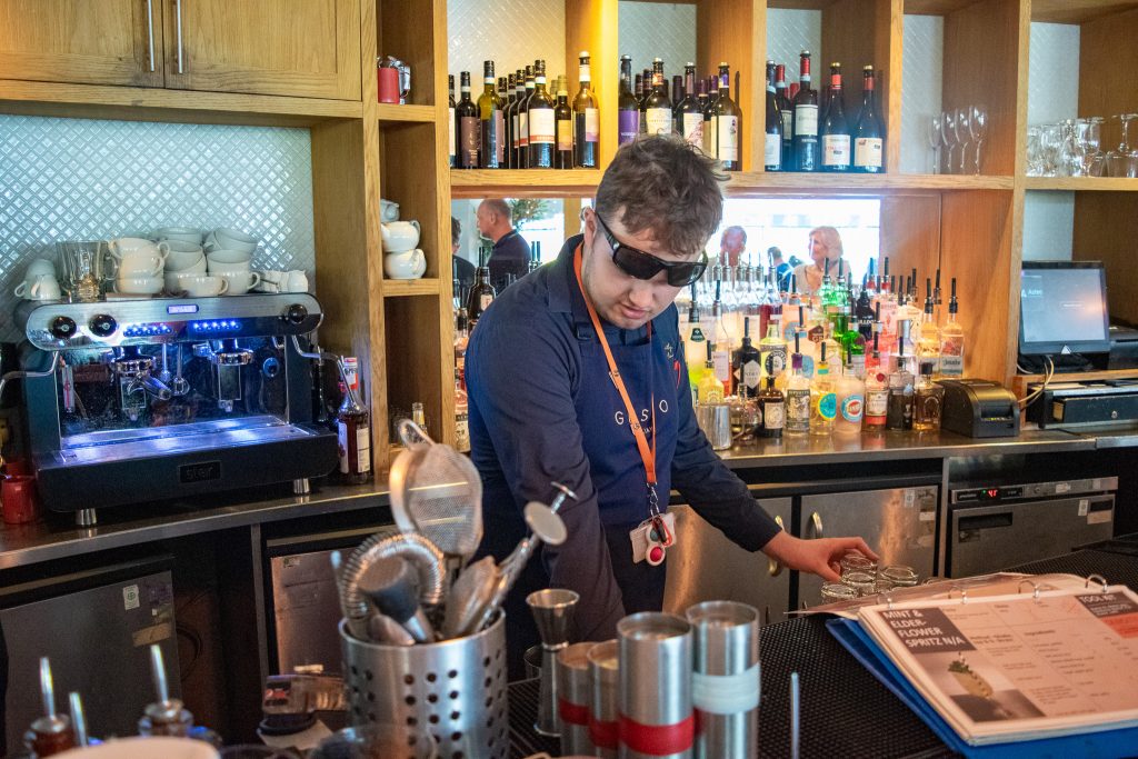 Teenage boy wearing uniform and sunglasses working at the restaurant bar.